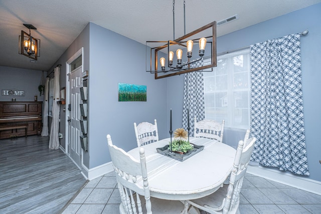 dining area featuring visible vents, a notable chandelier, a textured ceiling, light tile patterned floors, and baseboards