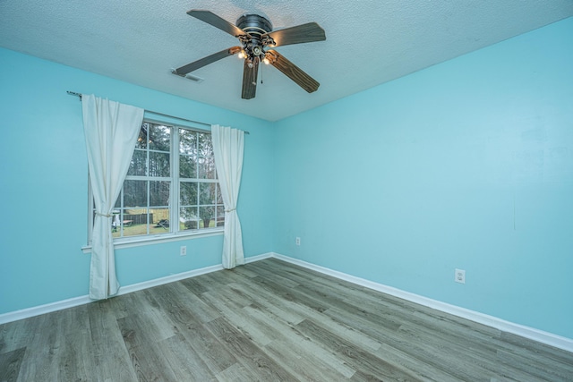 spare room with wood finished floors, visible vents, baseboards, ceiling fan, and a textured ceiling