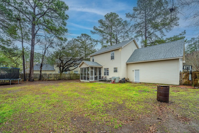 back of house featuring a shingled roof, a trampoline, fence, a lawn, and a sunroom