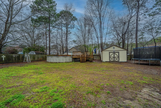 view of yard featuring a trampoline, a shed, a fenced backyard, a deck, and an outbuilding