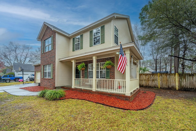 traditional-style home featuring brick siding, covered porch, a front lawn, and fence