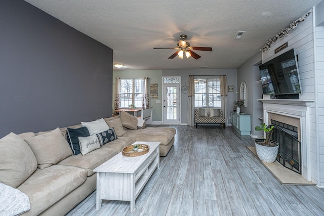 living area featuring a fireplace with raised hearth, a textured ceiling, wood finished floors, baseboards, and ceiling fan