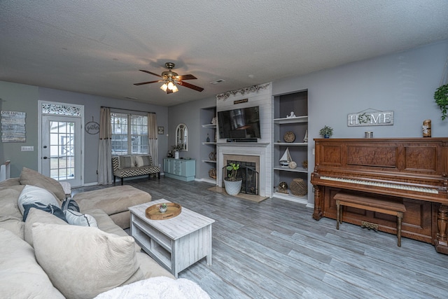 living area featuring a large fireplace, a textured ceiling, wood finished floors, and a ceiling fan