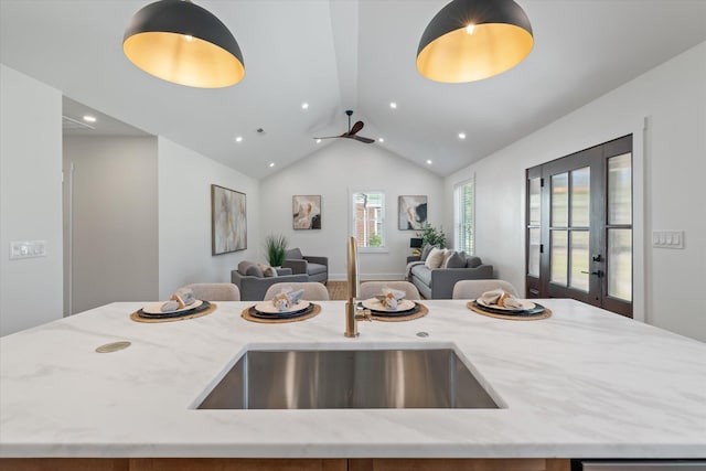 kitchen featuring lofted ceiling, light stone countertops, sink, and an island with sink