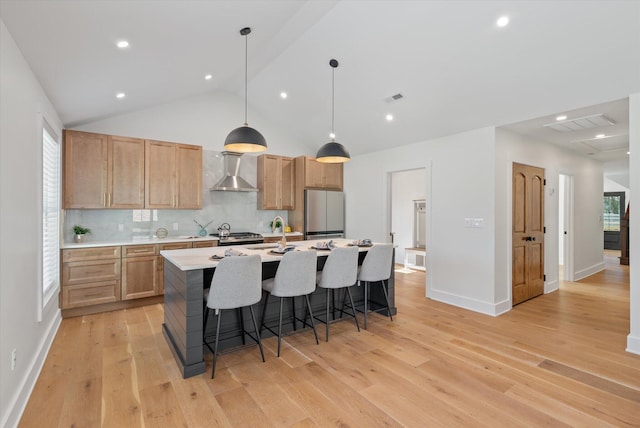 kitchen featuring vaulted ceiling, stainless steel refrigerator, light hardwood / wood-style flooring, wall chimney exhaust hood, and decorative light fixtures