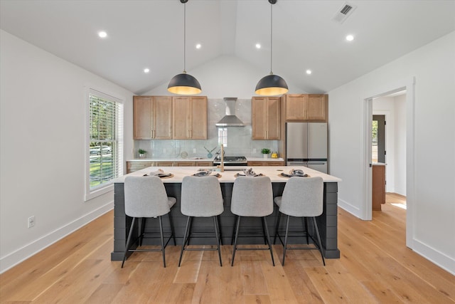 kitchen with appliances with stainless steel finishes, vaulted ceiling, pendant lighting, light hardwood / wood-style floors, and wall chimney exhaust hood