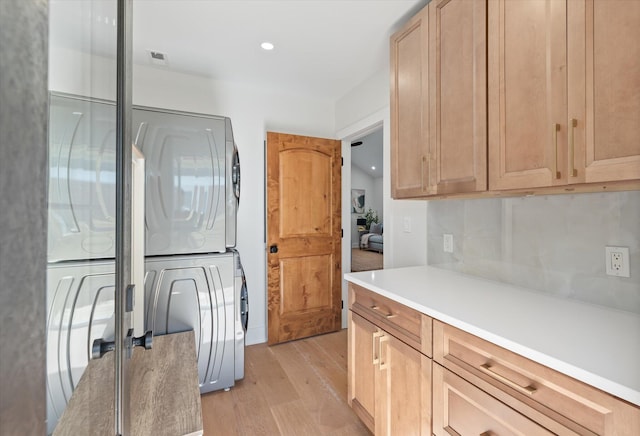 kitchen with stacked washer / drying machine, decorative backsplash, light wood-type flooring, and light brown cabinets