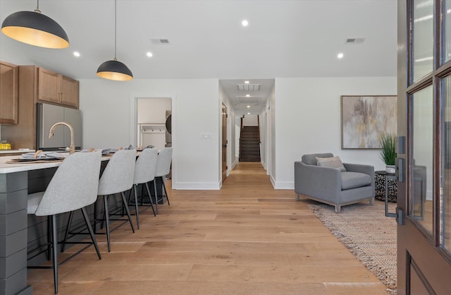 kitchen with stainless steel fridge, decorative light fixtures, light wood-type flooring, and a breakfast bar