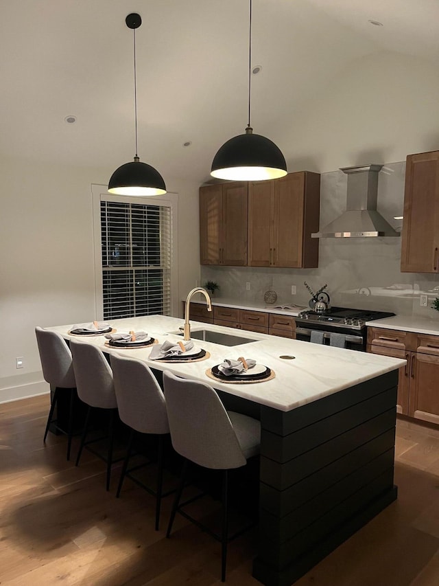 kitchen featuring wall chimney range hood, a kitchen island with sink, gas range, and sink