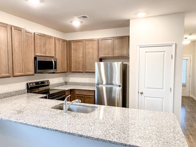 kitchen with kitchen peninsula, light stone countertops, light wood-type flooring, appliances with stainless steel finishes, and sink