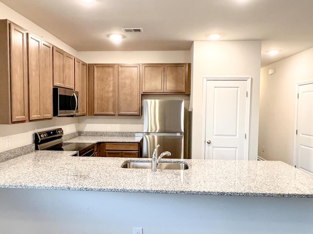 kitchen with sink, kitchen peninsula, light stone counters, and appliances with stainless steel finishes