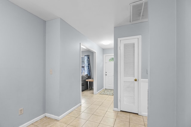 hallway with baseboards, visible vents, and light tile patterned floors