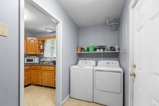 washroom with a sink, light tile patterned floors, separate washer and dryer, laundry area, and baseboards