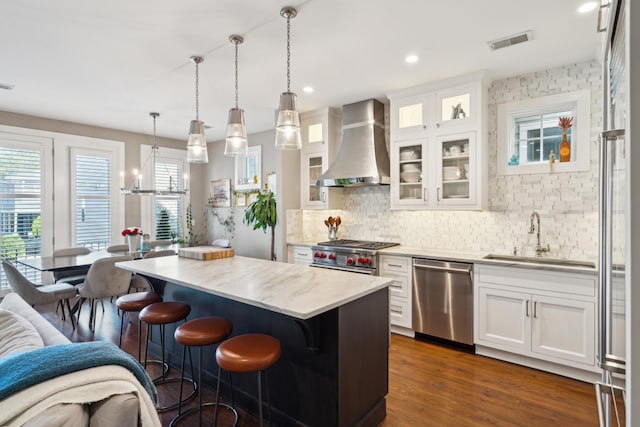 kitchen with pendant lighting, white cabinets, wall chimney exhaust hood, and stainless steel appliances