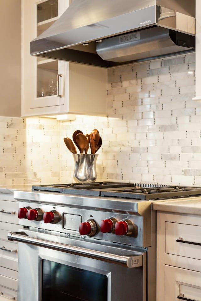 kitchen with backsplash, white cabinetry, ventilation hood, and premium stove