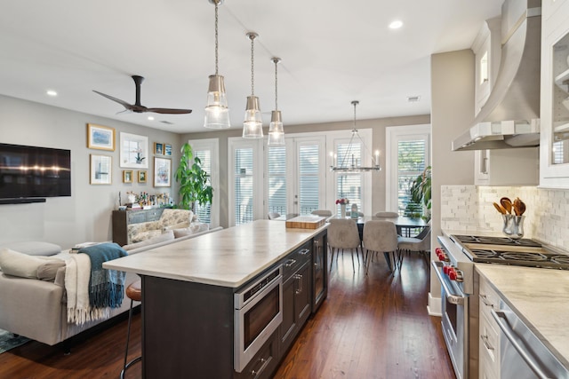 kitchen featuring appliances with stainless steel finishes, a kitchen island, wall chimney range hood, hanging light fixtures, and a breakfast bar area