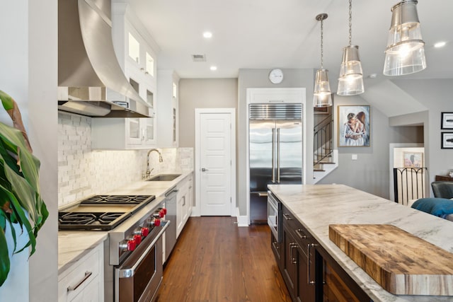 kitchen with light stone countertops, extractor fan, white cabinetry, high end appliances, and sink