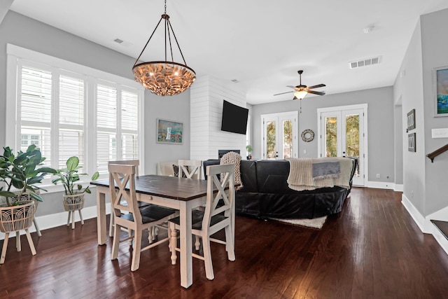 dining space featuring ceiling fan with notable chandelier, a large fireplace, french doors, and dark hardwood / wood-style floors