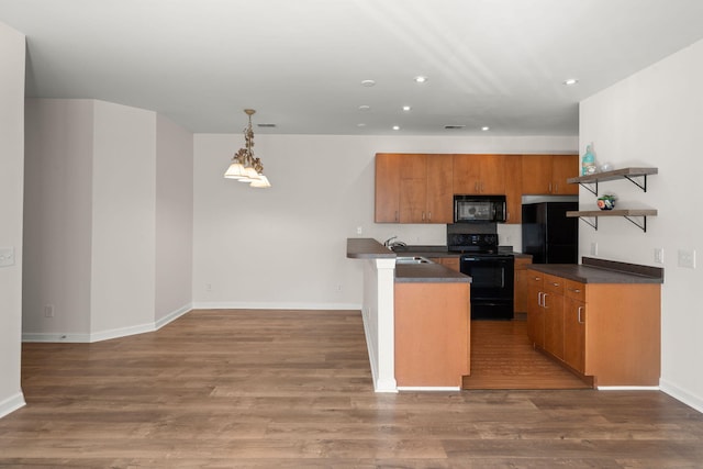 kitchen featuring sink, hanging light fixtures, wood-type flooring, a center island with sink, and black appliances