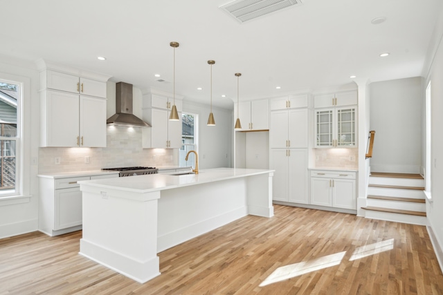 kitchen with white cabinets, a center island with sink, and wall chimney exhaust hood