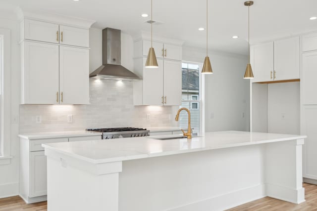 kitchen with a kitchen island with sink, sink, white cabinets, and wall chimney range hood