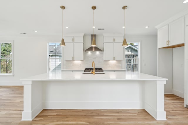 kitchen with white cabinetry, a large island, wall chimney exhaust hood, and decorative light fixtures