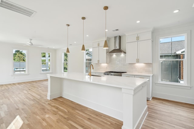 kitchen with white cabinets, wall chimney exhaust hood, sink, and a kitchen island with sink