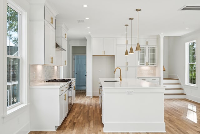 kitchen featuring decorative backsplash, white cabinets, a kitchen island with sink, and sink