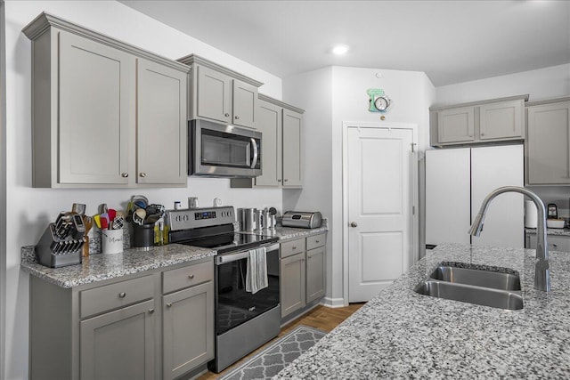 kitchen with sink, gray cabinets, light stone counters, dark hardwood / wood-style flooring, and stainless steel appliances