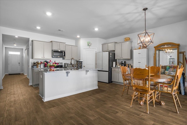 kitchen featuring gray cabinetry, dark wood-type flooring, refrigerator, and an island with sink