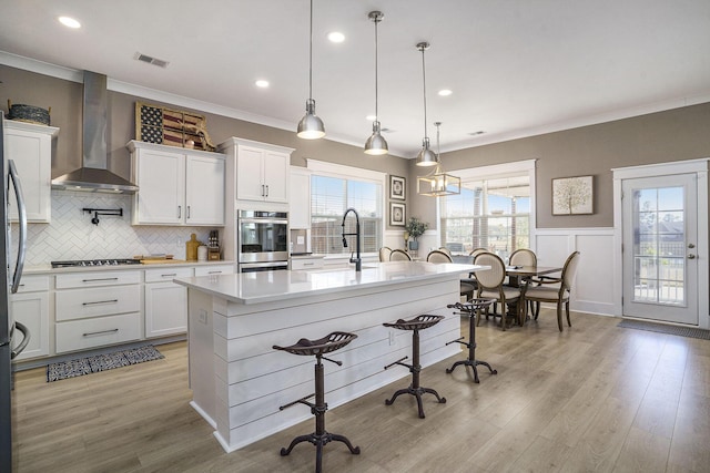 kitchen featuring visible vents, white cabinetry, light wood-style floors, wall chimney exhaust hood, and light countertops