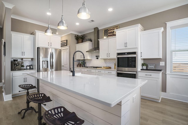 kitchen with visible vents, a breakfast bar, stainless steel appliances, wall chimney exhaust hood, and crown molding