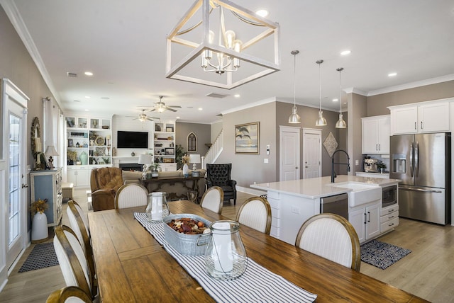 dining room featuring light wood finished floors, a lit fireplace, ornamental molding, and ceiling fan with notable chandelier