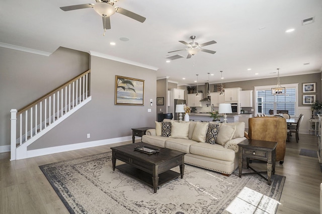 living area with visible vents, stairway, crown molding, and ceiling fan with notable chandelier