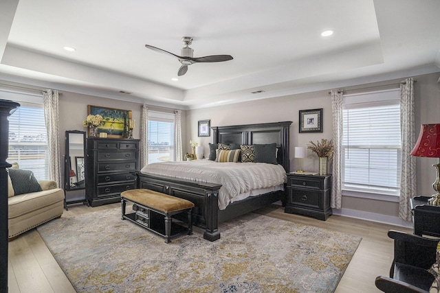 bedroom with a raised ceiling, multiple windows, and wood finished floors