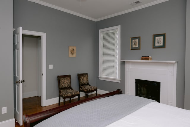 bedroom with wood finished floors, ornamental molding, a fireplace, baseboards, and visible vents