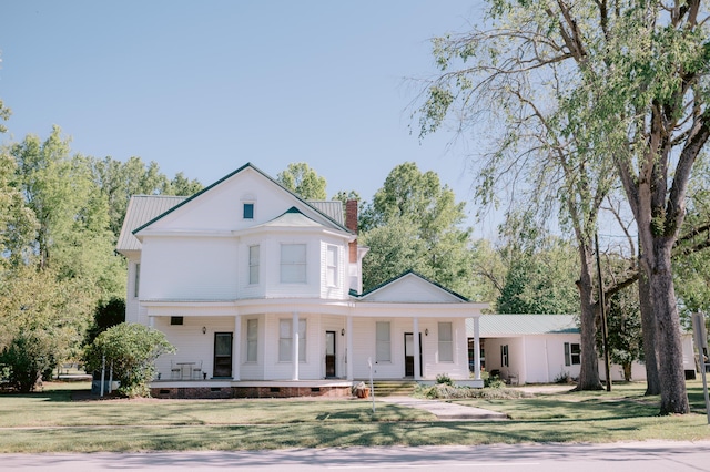 view of front facade featuring a chimney, covered porch, a front yard, and crawl space