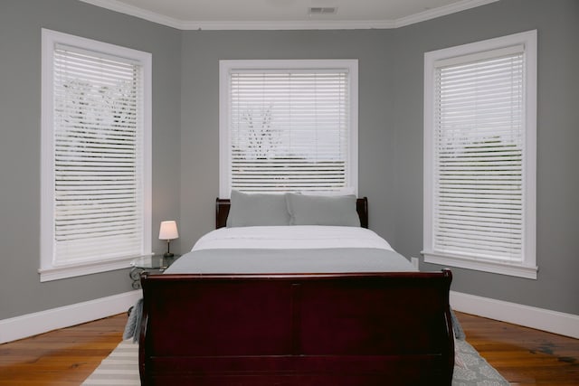 bedroom featuring ornamental molding, visible vents, wood finished floors, and baseboards