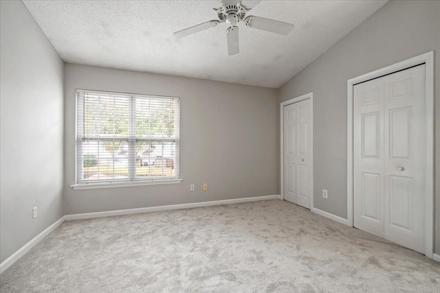 unfurnished bedroom with a textured ceiling, light carpet, lofted ceiling, two closets, and ceiling fan