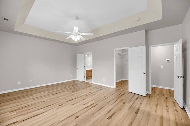 unfurnished bedroom featuring light wood-type flooring, a spacious closet, a tray ceiling, a closet, and baseboards