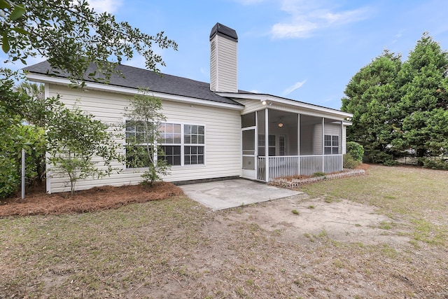rear view of property featuring a sunroom, a chimney, a patio area, and a yard