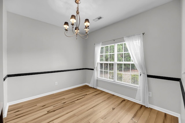 empty room featuring wood finished floors, a chandelier, and baseboards