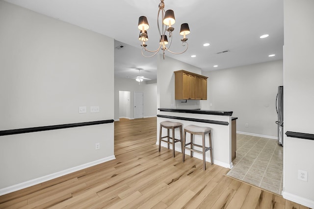 kitchen featuring freestanding refrigerator, light wood-type flooring, recessed lighting, baseboards, and a kitchen bar