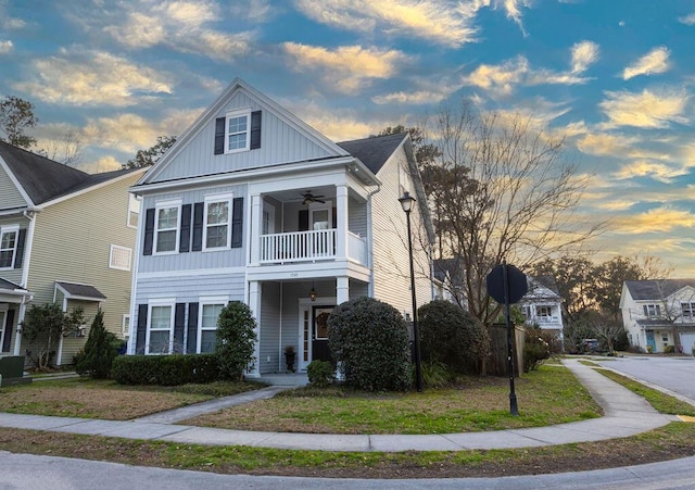 view of front of house with a lawn, board and batten siding, a balcony, and a ceiling fan