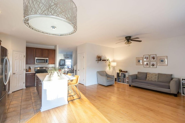 kitchen with light countertops, appliances with stainless steel finishes, open floor plan, light wood-type flooring, and a kitchen breakfast bar