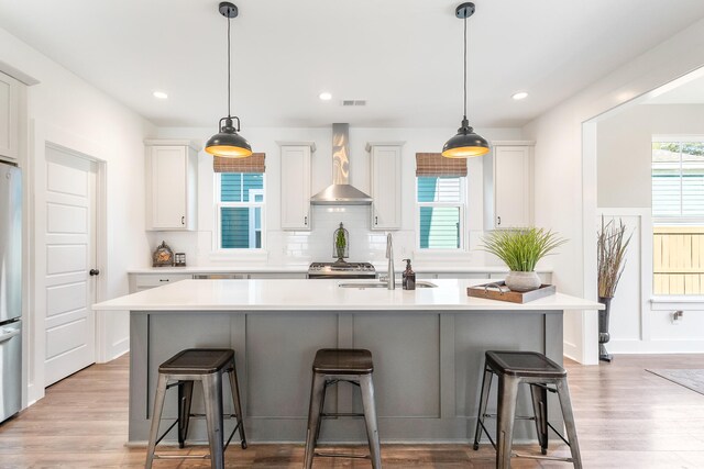 kitchen with a kitchen island with sink, wall chimney range hood, sink, and white cabinets