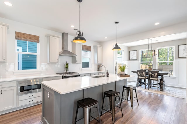 kitchen with pendant lighting, wall chimney exhaust hood, an island with sink, and hardwood / wood-style floors