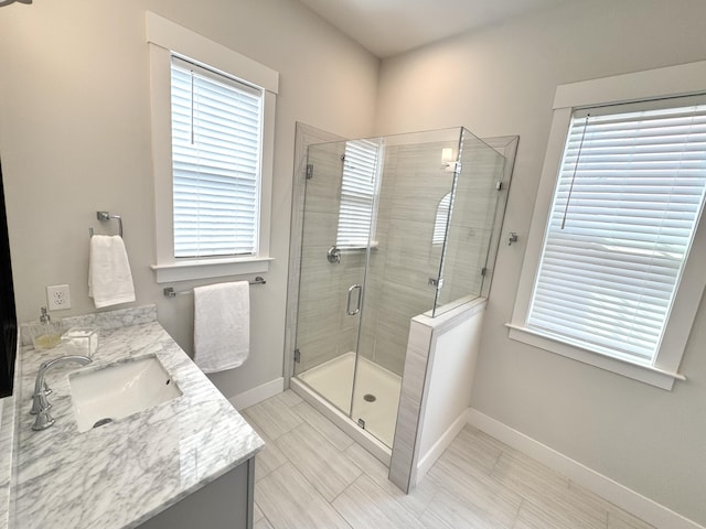 full bath with a healthy amount of sunlight, a shower stall, baseboards, and vanity