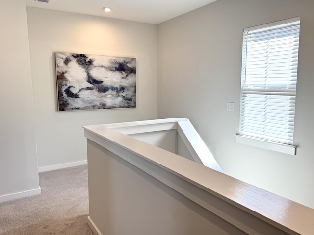 hall with carpet, baseboards, and an upstairs landing