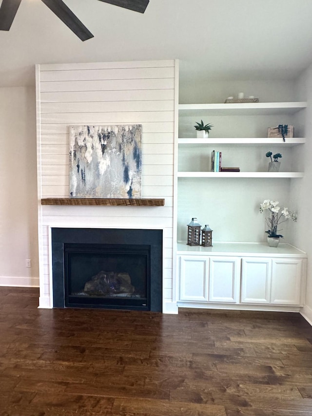 interior space with a large fireplace, ceiling fan, baseboards, and dark wood-style flooring